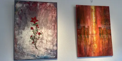 Två abstrakta målningar på väggen. Till vänster en röd blomma på en mörk bakgrund, en fin diy canvas. Till höger en stadssilhuett i varma färger.