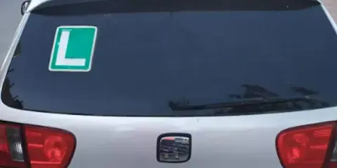 El coche tiene una L verde en la ventana trasera, indicando que el conductor está aprendiendo.