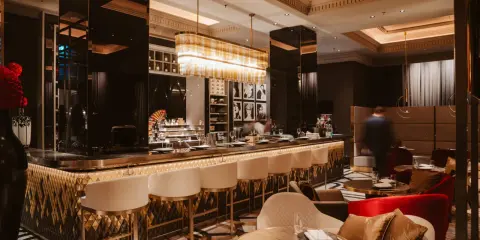 Elegante Bar mit goldenen Akzenten, weißen Barhockern und stilvollen Sitzbereichen. Ein Ort, der zu den besten Restaurants in Berlin passt.