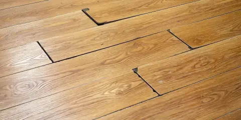 Suelo de madera con tablas levantadas y espacios oscuros, indicando posible daño por humedad. Se busca cómo quitar mancha negra humedad madera.