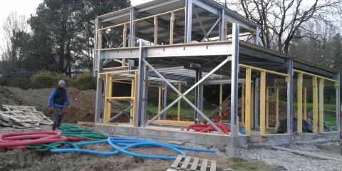 Chantier d'une maison ossature métallique. Le prix est un facteur clé pour ce type de construction moderne. Des tuyaux colorés sont visibles au sol.