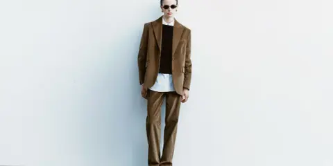 Model in a brown corduroy suit, white shirt, and black sweater, wearing sunglasses.