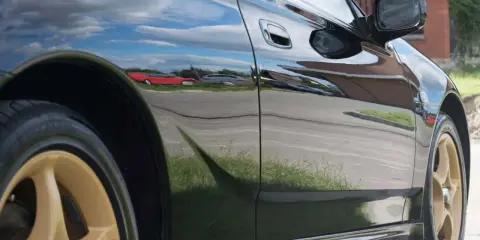 Błyszczący czarny lakier samochodu odbija chmury i inne pojazdy, tworząc efektowne hologramy na lakierze.