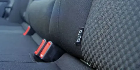 Etiqueta negra con el **símbolo ISOFIX** en el asiento de un coche, junto a los anclajes de seguridad.