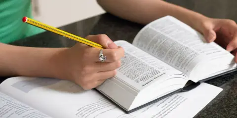 Mani che studiano un dizionario, scrivendo con una matita. Scoprire parole italiane affascinanti è un viaggio.