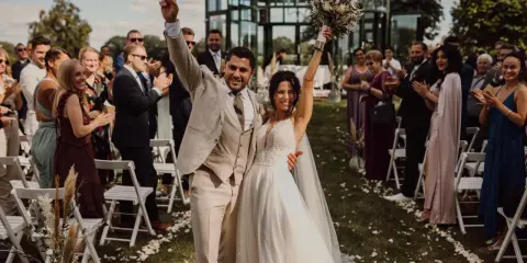 Glückliches Brautpaar feiert den Beginn des Hochzeitsablaufplans. Gäste applaudieren bei der Zeremonie im Freien.