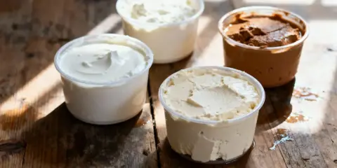 Composition de quatre pots de produits laitiers crémeux, dont une ricotta au chocolat, sur une table en bois rustique.