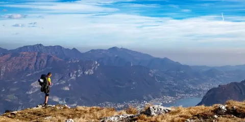 Escursionista ammira la vista panoramica di una montagna vicino Milano, con un lago e un paese in lontananza.