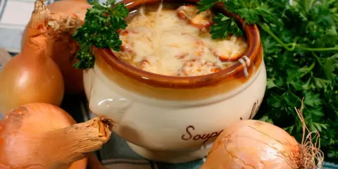Un bol de soupe à l'oignon gratinée, un plat parisien réconfortant, entouré d'oignons frais et de persil.