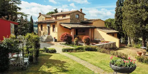 Un perfetto weekend in Toscana: villa con giardino fiorito, cipressi e un cielo azzurro con nuvole bianche.
