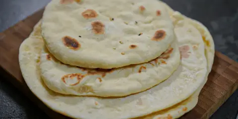 Pile de pains arabes moelleux, légèrement dorés par la cuisson, sur une planche en bois. Parfait pour accompagner un repas.