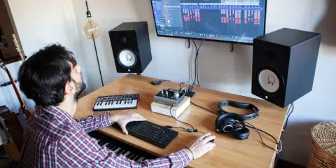 Un homme crée de la musique dans son studio. Il utilise un clavier, un ordinateur et des enceintes pour apprendre comment écrire un son.