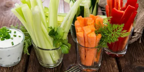 Geschnittene Karotten, Sellerie, Gurken und Paprika in Gläsern, dazu ein Dip. Perfekte Snacks nach dem Sport für gesunde Erholung.