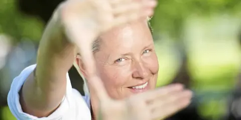 Regina Lund ler inramad av sina händer, som om hon skapar en scen för en film.