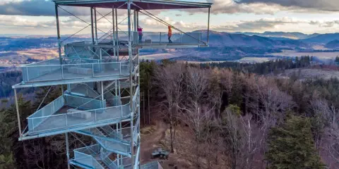 Trójgarb wieża widokowa oferuje wspaniałe widoki na okoliczne wzgórza i lasy. Dwie osoby podziwiają panoramę z platformy widokowej.