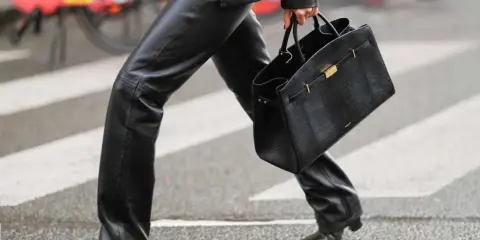 A person walks across a crosswalk in a chic leather pants outfit, perfect for winter. They carry a stylish black handbag.