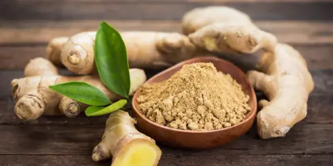 Des racines de gingembre frais et de la poudre de gingembre dans un bol en bois. Le gingembre est-il aphrodisiaque ? Une question qui suscite la curiosité.