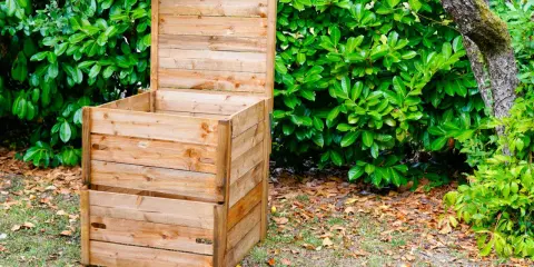 Un composteur en bois, prêt à l'emploi, est installé dans un jardin verdoyant. Idéal pour fabriquer un composteur maison.