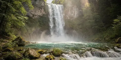 Cascata maestosa nei Laghi di Plitvice, con acqua turchese e rocce muschiose. La luce solare filtra tra gli alberi, creando un'atmosfera magica.