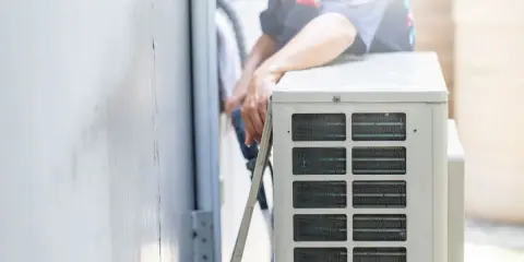 Un technicien s'occupe de recharger la clim de la maison. Il manipule des tuyaux près de l'unité extérieure.