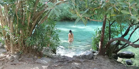 Una mujer se baña en la cueva del gato, un oasis de aguas cristalinas rodeado de vegetación exuberante.