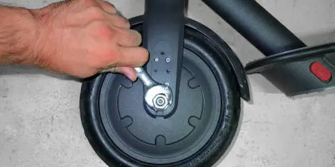 Main tenant utilise une clé pour changer la roue avant d'une trottinette électrique.