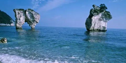 La **Baia delle Zagare** con le sue iconiche faraglioni bianchi che emergono dal mare blu intenso, sotto un cielo limpido.