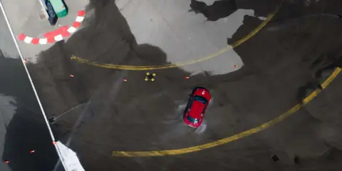Auto rossa in derapata su asfalto bagnato, con coni arancioni e segnali di pista. I pneumatici Kumho mostrano i loro limiti in condizioni difficili.