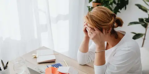 Zmartwiona kobieta przy biurku z rachunkami i kalkulatorem. Zastanawia się, ile kosztuje pozew o alimenty u adwokata.