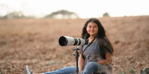 Młoda kobieta z aparatem na statywie, siedząca na ziemi. Kompozycja wertykalna przykłady dla fotografów przyrody.