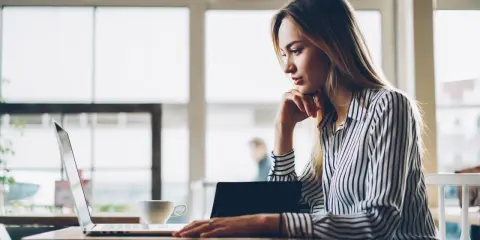 Donna pensa a come fare un webinar, seduta al laptop con una tazza di caffè.