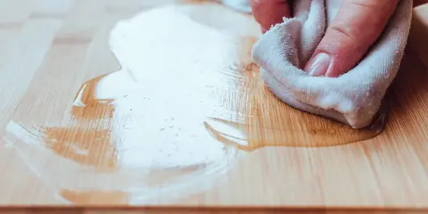 Mano limpiando pintura del suelo de madera con un trapo.