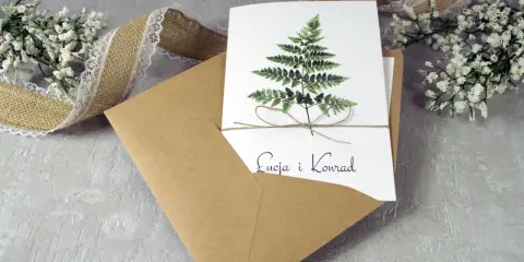 Eleganckie zaproszenie ślubne z paprocią i imionami pary. W zestawie koperta i ozdobna wstążka. To, co musi zawierać zaproszenie, to jego piękny design.