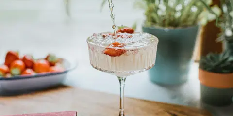 Un cocktail sans alcool surprenant, avec des fraises fraîches, est préparé. Des plantes vertes en arrière-plan ajoutent une touche de nature.