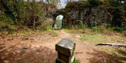 Kamienny postument przed łukiem w fort karola. Ścieżka prowadzi przez zarośla do zabytkowej budowli.
