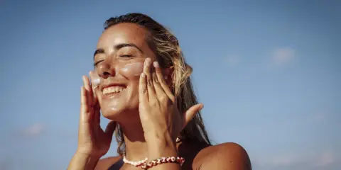 Donna sorridente applica crema solare per proteggere la pelle da macchie e tumore.