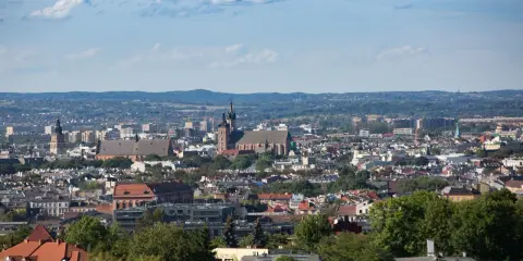Widok na Kraków z punktu widokowego. W oddali widać kościół Mariacki i Wawel, a bliżej zabudowania miejskie i zieleń.