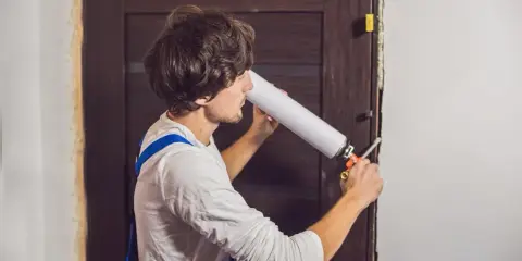 Un homme en salopette bleue utilise une mousse expansive pour comment isoler une porte.