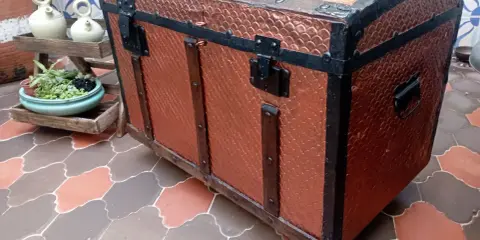 Un baúl antiguo restaurado, con detalles metálicos y acabado en cobre texturizado, listo para guardar tesoros.