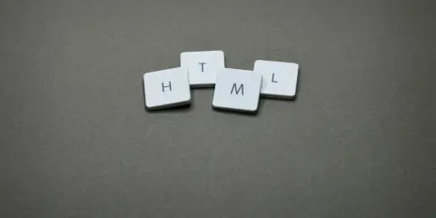 Białe kafelki z literami H, T, M, L ułożone na szarym tle, tworząc słowo HTML.