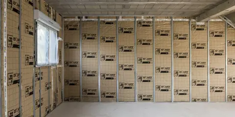 Le chantier progresse, on commence à isoler un mur avec des panneaux Isover. Une fenêtre est visible sur la gauche.