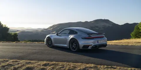 Silberner Porsche 911 Turbo S, ein Sondermodell 2023, parkt auf einer Bergstraße mit sanften Hügeln im Hintergrund.