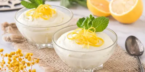 Dos copas de cremoso mousse de limón con leche condensada, decoradas con ralladura de limón y menta.