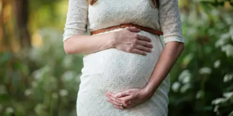 Kobieta w białej sukience obejmuje ciążowy brzuch. To piękny moment, kiedy można zajść w ciążę i poczuć nowe życie.