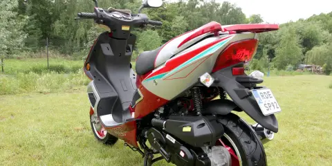 Czerwony skuter 50cc na trawie. Zastanawiasz się, ile jedzie skuter 50 bez blokad? Ten model wygląda na gotowy do szybkiej jazdy!