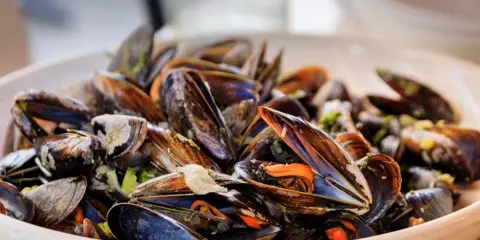 Un plato rebosante de mejillones al vapor, con sus conchas abiertas mostrando la carne anaranjada y jugosa.