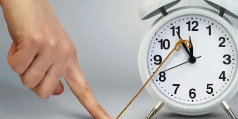 Dłoń próbuje zatrzymać czas, łapiąc sznurkiem wskazówkę budzika.