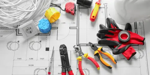 Outils d'électricien sur un plan : fils, prises, tournevis, pinces, marteau, casque et gants pour installer le courant électrique.
