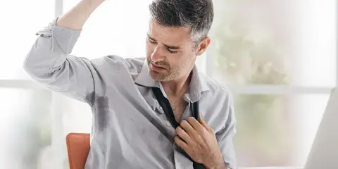 Uomo d'affari con camicia bagnata di sudore sotto le ascelle, che si sbottona la cravatta. Le cause del sudare freddo sono molteplici.