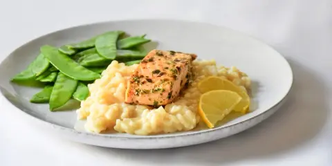 Ein Stück Lachs auf cremigem Zitronenrisotto, garniert mit Zuckerschoten und Zitronenspalten.